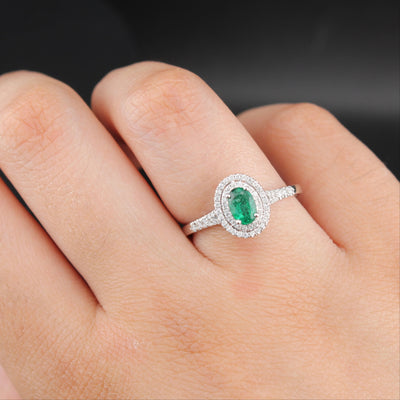 Silver ring with a green gemstone on a finger against a dark background